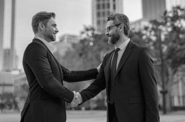 Amerikalı işadamı ortağıyla tokalaşıyor. Takım elbiseli işadamları dışarıda el sıkışıyor. İş fikri. Müşteri ile iş ilişkisi. İki işadamı arasındaki el sıkışma.