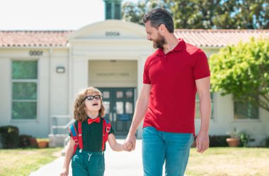 Baba oğluna okula kadar eşlik ediyor. Sırt çantalı ilkokul öğrencisinin ebeveyni ve öğrencisi.