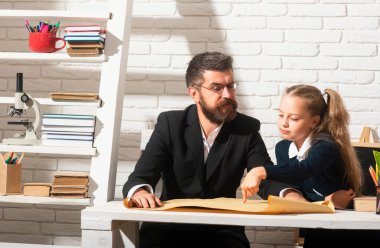 Sınıfta ciddi bir öğretmeni olan ilkokul öğrencisi kız. Babalar ve kızları öğreniyor. Babamla ödev yapıyorduk.