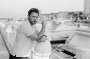 Büyük şehirde kendine güvenen yakışıklı bir adamın portresi. Sokakta poz veren sıradan giyinmiş seksi bir adam. Şehir yaşam tarzında başarılı bir erkek model. Yatın yanında zengin bir adam hayal ediyor.