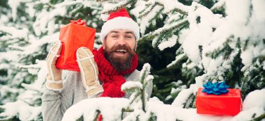 Kuzey Kutbu 'nda hediye kutusuyla mutlu bir Noel Baba portresi. Noel hediyeli mutlu adam dışarıda. Karlı kış arkaplanı. Mutlu Noel Baba 'nın dışarıda kar yağarken çekilmiş fotoğrafı. Elinde hediyeler var.