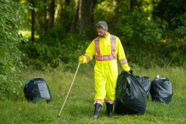 Üniformalı adam temizlik için çöp plastiği topluyor. Çöpleri toplayan adam. Çöp şişeleri toplandı. Plastik atık. Çöp toplama, çevre. Ekoloji, kirlilik, plastiklerden temizlik