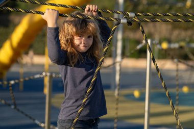 Çocuk çocuk oyun parkındaki halat ağına tırmandı. Çocuk ağa tırmanıyor. Çocuklar güneşli yaz gününde dışarıda oynar ve tırmanırlar.
