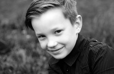 Tarz sahibi, siyah tişörtlü, çimen arka planda gülümseyen çocuk.