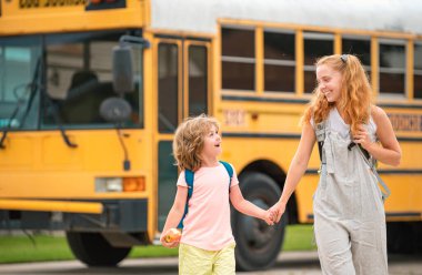 Okula dönelim. Okul otobüsündeki ilkokul öğrencileri. Çalışmaya biraz hazır. Mutlu küçük kız ve erkek kardeş okul otobüsünün önünde yan yana duruyorlar.