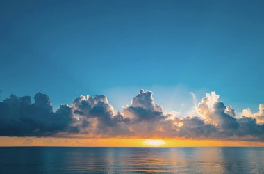 Gökyüzü ve bulutların arasından güneş batarken deniz batıyor. Okyanus ve gökyüzü arkaplanı, deniz manzarası.