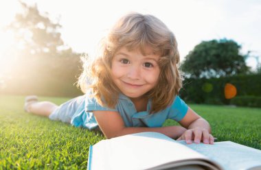 Çimlerin üzerinde kitap okuyan sevimli çocuk. Çocuk yaz parkında kitap okuyor.