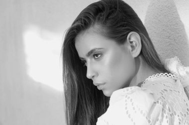 Genç ve şık bir kadının yakın çekim yüzü. Beyaz duvar arkasında güzel bir kız, açık hava portresi.