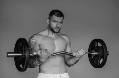 Seksi kaslı adam kaslarını şişiriyor ve spor salonunda halteri kaldırıyor. Halterle egzersiz yapan formda bir adam. Kaslı genç yakışıklı adam ağırlık kaldırıyor. Ağırlık kaldırma ve halterle antrenman