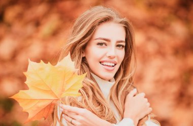 Sonbahar parkında gülen bir kadın. Moda kıyafetli, güzel, kaygısız, kıvırcık kız gülümseyerek dinleniyor. Parktaki komik sarışın portre, sonbahar konsepti. Dışarı çık.