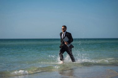 Leisure weekend and remote freelance work. Crazy comic business man in suit rest on sea bech. Funny businessman with laptop runnig on water. Remote summer business. Summer holiday for businessman