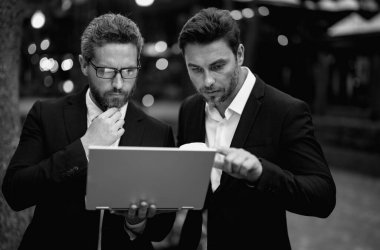 Takım elbiseli yakışıklı bir iş adamı laptopta çalışıyor ve şehirdeki iş projeleriyle iletişim kuruyor. Ortaklar iş için düşünür ve plan yapar. İki iş adamı dışarıda tablet laptop kullanıyor.