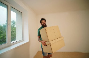 Komik adam eşyalarını kutularda taşıyor. Yeni bir daireye taşınıyorum. Karton kutuları olan mutlu genç bir adam. Taşındığı gün kutuları taşıyan adam.