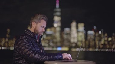 Ceketli bir iş adamı gece vakti telefonda dizüstü bilgisayar kullanarak konuşuyor. New York 'un dışında çalışan olgun bir iş adamı. İş görüşmesinde dizüstü bilgisayarı ve telefonu olan bir iş adamı