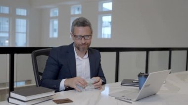Para kazan. İş adamı ofiste dolar sayıyor. Takım elbiseli bir ofis çalışanı ve dolar. Ofis işvereni para banknotlarını tutar. Takım elbiseli adam dolar sayıyor. Para ver, para kazan.