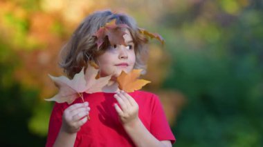 Sonbahar parkında yaprakları olan bir çocuk. Çocuk dışarıda eğleniyor. Sonbaharın tadını çıkarıyorum. Arka planda kal. Sonbahar ormanı arka planında güzel bir sonbahar çocuğunun portresi. Güzel çocuk düşen yapraklarla oynuyor.