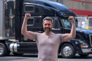 Mutlu kamyon şoförü. CDL. Kamyon aracının yanında nakledilmeye hazır duran kamyoncu portresi. Kamyonun önünde duran bir erkek sürücü.