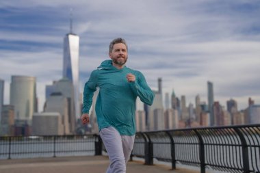 Dışarı koş. Sokakta koşan bir adam. Olgun koşucu ve spor modelleri New York 'ta Manhattan yakınlarında antrenman yapıyor. Milenyum sporcusu. Spor eğitimi açık havada.