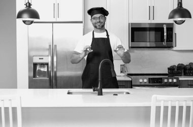 Mutfakta şef üniforması giyen yakışıklı orta yaşlı bir adam. Aşçılık ve aşçılık. Restoran menüsü konsepti. Yemek servisi, yemek pişirme, yemek reklamcılığı. Üniformalı adam mutfakta.