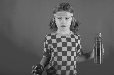 Sportif çocuk. Kid 'in portresi şişede su ve elma tutuyor. Stüdyonun sarı arka planında spordan sonraki çocuk. Fitness çocukları. Sağlıklı çocuk aktif yaşam tarzları