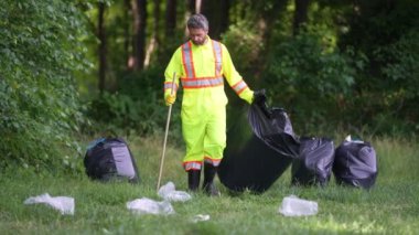 Adam parkı temizliyor, çöpü çöp torbasına koyuyor. Çevresel koruma. Temizlik için çöp poşeti topluyorum. Çöp poşetine çöp poşeti koymak. Kirlilik ve geri dönüşüm.