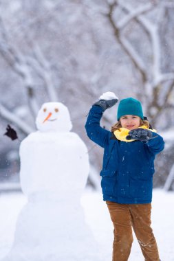 Mutlu Çocuk kışın kardan adam için kartopu yapıyor. Çocuk karda oynuyor. Açık havada aktif kış oyunları. Çocuk karla oynarken eğleniyor. Çocuklar için açık havada kış tatili. Güneşli kış gününde çocuk oyunu