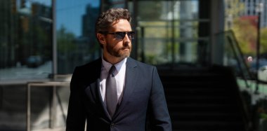 Modern ofis binasının önünde duran kendine güvenen bir iş adamı. İş başarısı. Dışarıyı düşünen bir iş adamı. Takım elbiseli modern iş adamı ofis manzarasının yanında duruyor.