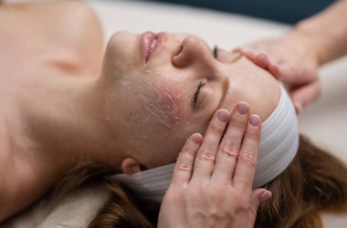 Güzellik tedavisi. Estetik kozmetoloji, yüz bakımı. Yüz bakımı. Yüz kilinden maske takan spa kadını, yakın plan. Güzellik kliniğinde cilt masajı. Güzellik kozmetolojisi