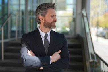 Modern ofis binasının önünde duran kendine güvenen bir iş adamı. İş başarısı. Dışarıyı düşünen bir iş adamı. Takım elbiseli modern iş adamı ofis manzarasının yanında duruyor.