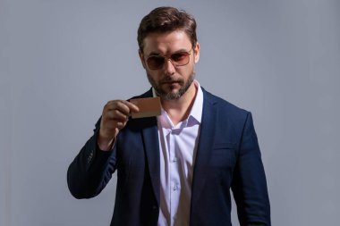 Stüdyonun gri arka planında kredi kartı tutan bir iş adamı. Kredi kartı olan bir iş adamı, banka indirimi öneriyor. E-bankacılık, e-ticaret, para transferi için kredi kartı