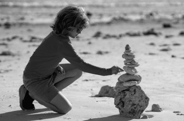 Sakin çocuk yaz kumsalında piramit taşlarıyla oynuyor. Çocuk taş yığınıyla oynuyor. Çocuk sahilde oynuyor. Denge ve çocuklar uyum konsepti. Yaz tatilinde çocuk oyunu