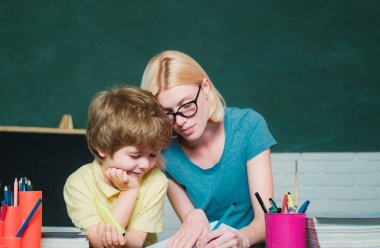Komik küçük çocuk ve genç kadın öğretmen kara tahta arka plan üzerinde eğleniyor. Okulda ki kadın öğretmen ve okul çocuğu. Büyük çalışma başarısı