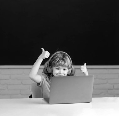 Kulaklıklı zeki çocuk masada oturur, okulda dizüstü bilgisayarda çalışır, klever çocuk internet derslerini kullanarak not defterinde kulaklık takar. Okuldaki ilk günüm.