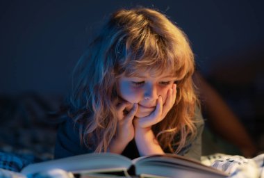 Yatakta uzanmış kitap okuyan sevimli bir çocuk. Çocuk yatmadan önce kitap okuyor. Hayal gücü ya da öğrenme kavramı