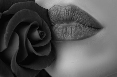 Beautiful young fashion woman with red lipstick. Glamour fashion model with bright gloss make-up posing at studio. CLoseup beauty portrait with a flower. Red rose. Beautiful woman lips with rose