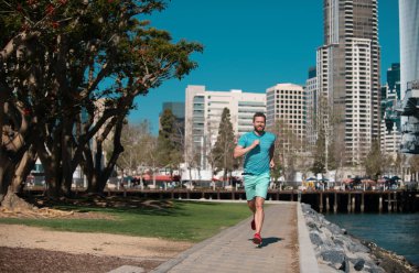 Atletik genç koşucu. Şehir sporları. Adam güzel bir yaz gününde şehirde koşuyor, koşuyor.