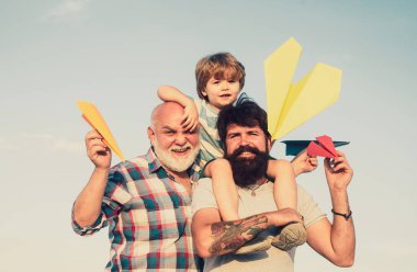 Babalar Günü. Büyükbaba, baba ve oğul kucaklaşıp birlikte eğleniyorlar. Gökyüzü arka planında oyuncak jetpack 'i olan çocuk pilot. Heyecanlı