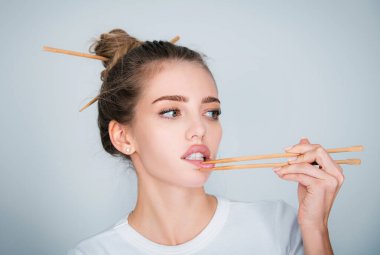 Suşi barındaki seksi genç kadın yemek çubuklarıyla dudaklarına dokunuyor. Suşi reklamı.