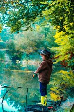 Çocuk balık tutmayı öğreniyor, gölde çubuk tutuyor. Elinde olta olan çocuk. Amerikalı çocuklar