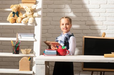 Okul üniforması giyen ve egzersiz kitabı tutan gülümseyen öğrenci kız. Okuldaki ilk günüm. Şirin küçük çocuk ders çalışıyor.