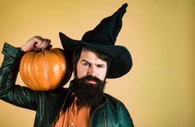 Cadılar Bayramı şapkasıyla balkabağı pişiren sakallı adam. Cadılar Bayramı afişi için tasarım. Elinde balkabağı olan yakışıklı bir cadılar bayramı erkeği. Çılgın şakacı surat. Balkabağıyla gülümseyen mutlu adam