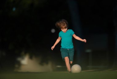 Futbol oynayan bir çocuk, mutlu bir çocuk, spordan hoşlanan bir çocuk, çocuk aktiviteleri, küçük bir futbolcu. Çocuk parkta futbol oynuyor.