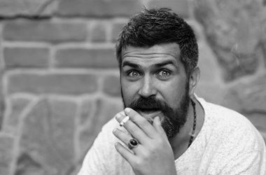 Sigara içen heyecanlı bir adam. Sakallı adam tuğla duvara karşı sigara içiyor.