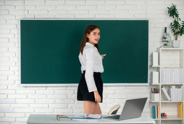 Genç, kendinden emin ve çekici bir kız öğrencinin portresi. Elinde tebeşirle okul arkaplanında duruyor.