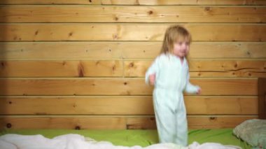 Pijamalı bebek gülüyor ve eve yatağa atlıyor. Çocukluk, günaydın. Bebek yatakta zıplıyor, evde eğleniyor. Çocuk zıplayarak ve yatakta oynayarak eğleniyor. Yatak odasında bebek oyunu