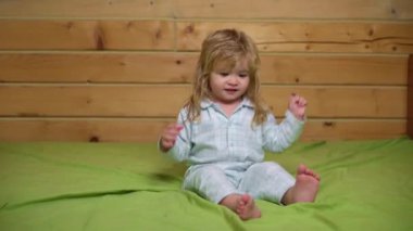 Pijamalı bebek gülüyor ve eve yatağa atlıyor. Çocukluk, günaydın. Bebek yatakta zıplıyor, evde eğleniyor. Çocuk zıplayarak ve yatakta oynayarak eğleniyor. Yatak odasında bebek oyunu