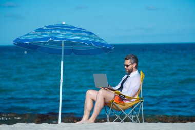 Çılgın özgür iş adamı. Eğlenceli iş hayatı. Deniz sahilinde dizüstü bilgisayarı olan yakışıklı bir iş adamı. Komik iş adamı. Serbest konsept, yaz işi. İş başarısı