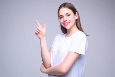 Kopya alanını gösteren genç bir kadın. Nokta. Kameraya bakan ve gri izole edilmiş arka plana bakan kızın stüdyo portresi. Parmak ucu hareketleri