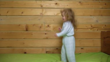Pijamalı bebek gülüyor ve eve yatağa atlıyor. Çocukluk, günaydın. Bebek yatakta zıplıyor, evde eğleniyor. Çocuk zıplayarak ve yatakta oynayarak eğleniyor. Yatak odasında bebek oyunu
