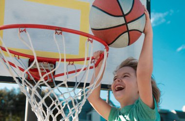 Basketbol sahasında basketbol maçında smaç yapan çocuk basketbolcunun yakın plan görüntüsü. Çocuk oyuncu spor giysileri giyiyor.